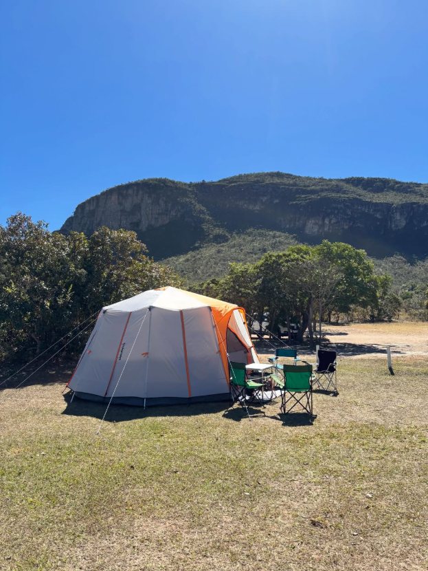 Barraca grande montada no gramado do camping, com cadeiras e o paredão da Chapada ao fundo
