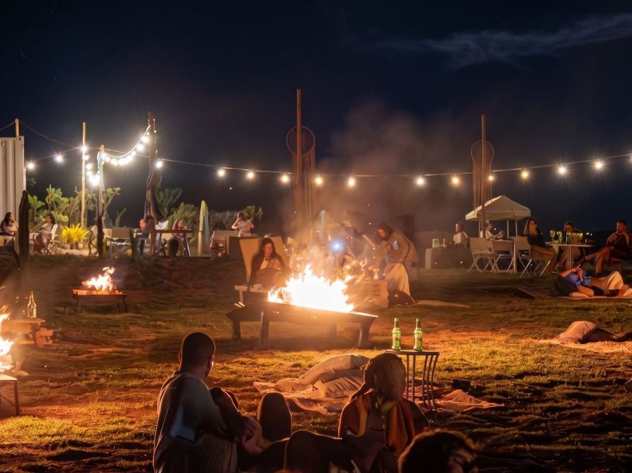 Noite de celebração ao ar livre com fogueiras, varal de luzes e céu escuro